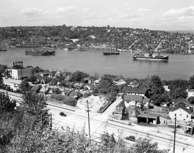 Black-and-white view from Queen Anne Hill across Lake Union toward Seattle, with houses, roads, docks, and ships along the waterfront — the neighborhood where Jack grew up.