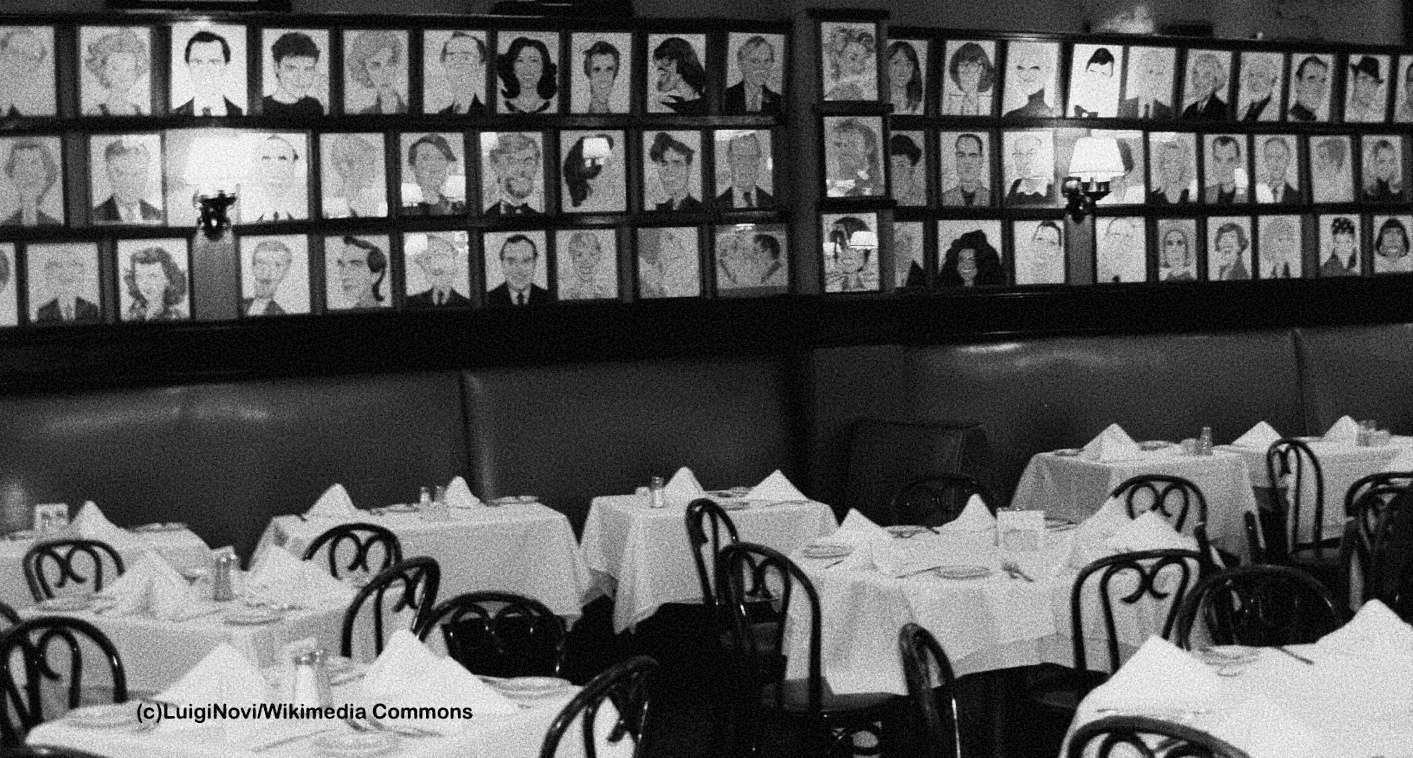 Black-and-white photograph of the dining room at Sardi's in New York City, its walls covered with rows of framed celebrity caricatures above the tables.