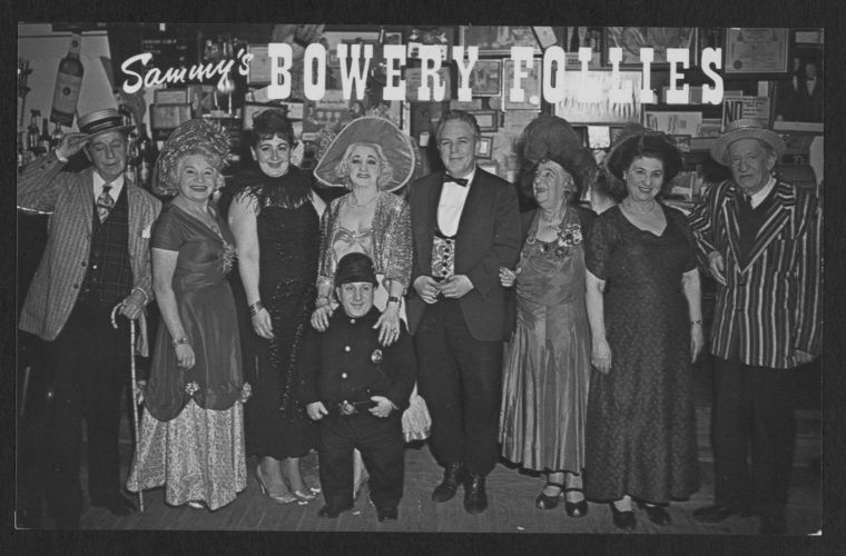 Black-and-white photograph of performers and staff at Sammy's Bowery Follies in New York City, posed beneath the club's large sign.