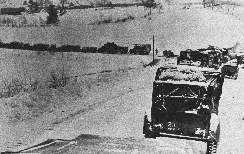 Black-and-white photograph of American military vehicles backed up along a narrow, snow-covered road near St. Vith, more vehicles visible across the countryside.