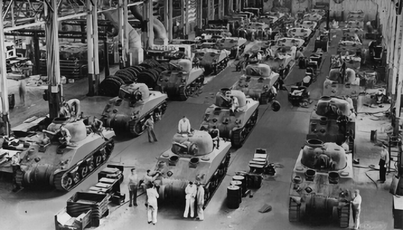 Black-and-white photograph of a wartime factory assembly line filled with rows of Sherman tanks in various stages of production, workers on and around the vehicles.
